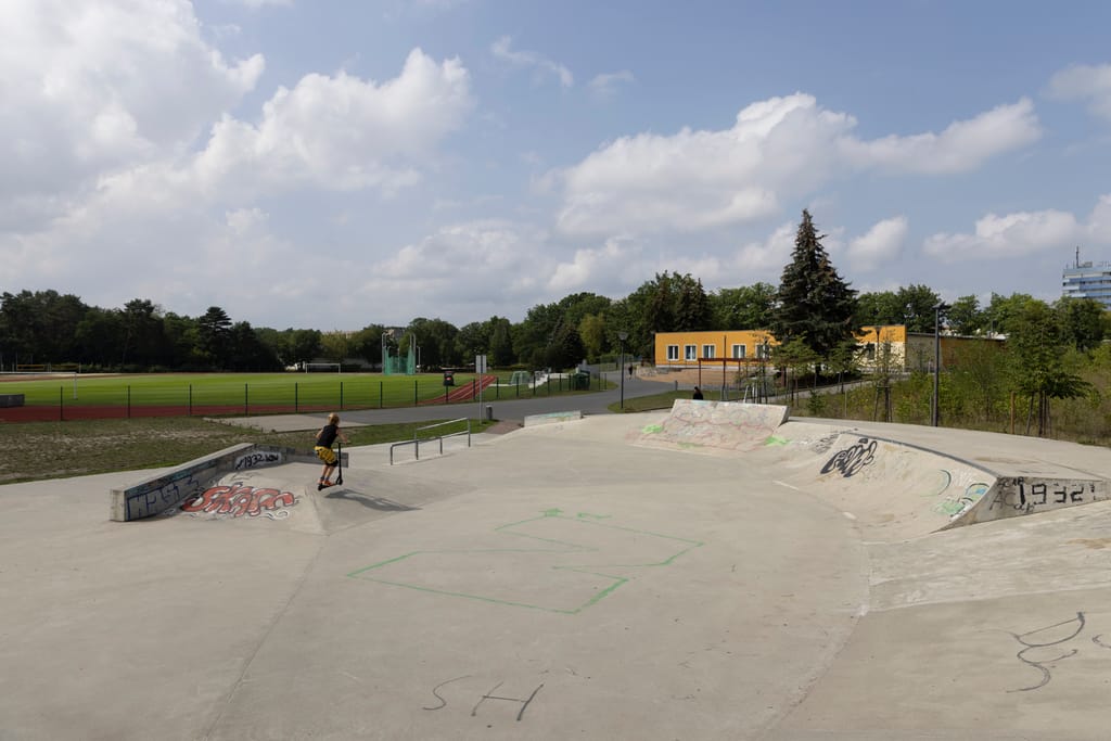Ein verlassener Skatepark. Auf die Rampen wurde teilweise Graffiti gesprüht und im Hintergrund sind moderne, große Gebäude zu sehen.